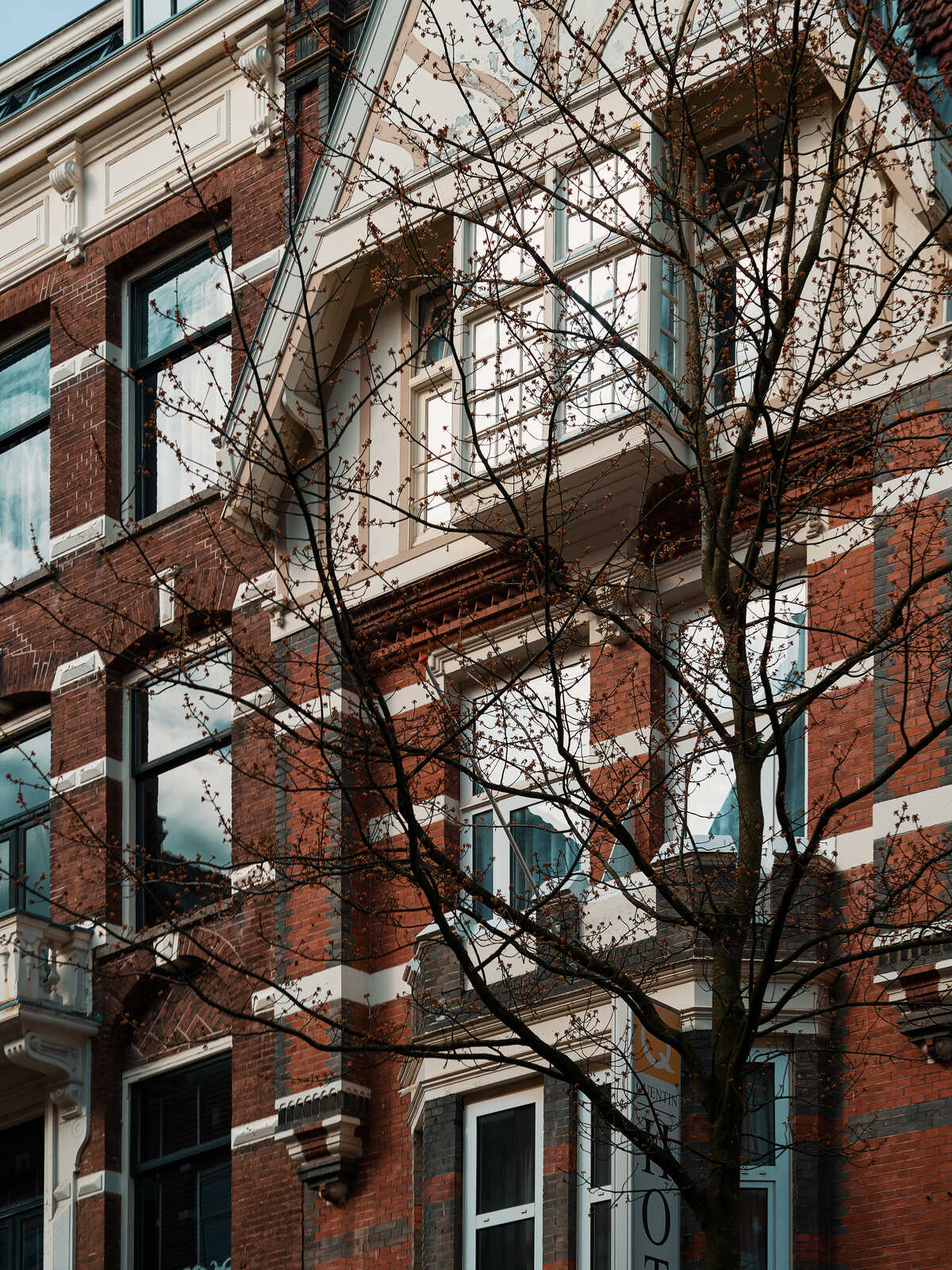 Red brick building with white decorative trim and bay windows. Bare tree branches frame the facade, against a cloudy sky.