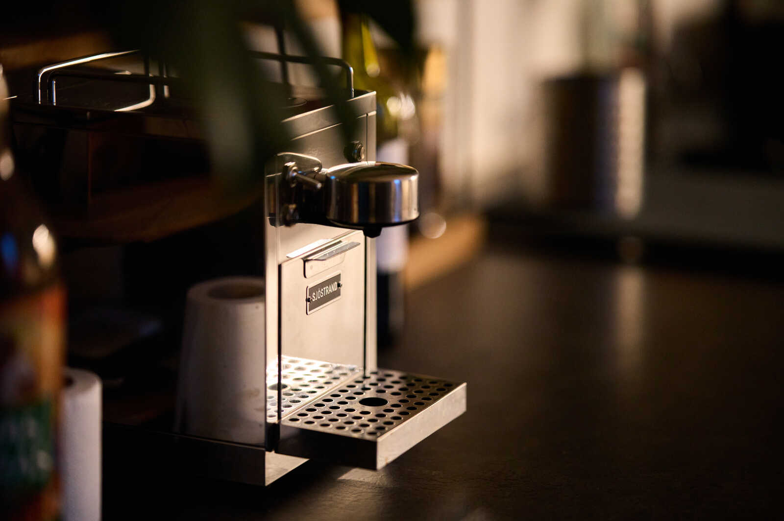 A silver espresso machine sits on a black countertop, with a drip tray below. A roll of paper sits next to it. The shot is taken at a close range.