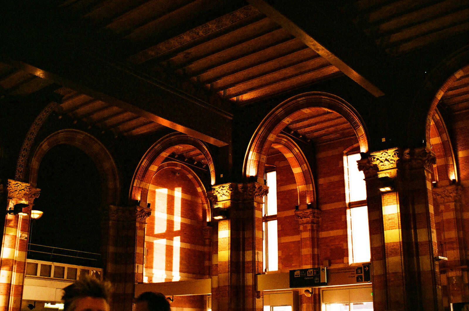 Arched windows with decorative columns and intricate carvings. Red brick facade with a dark upper level. Signage visible. Interior is illuminated with warm light.
