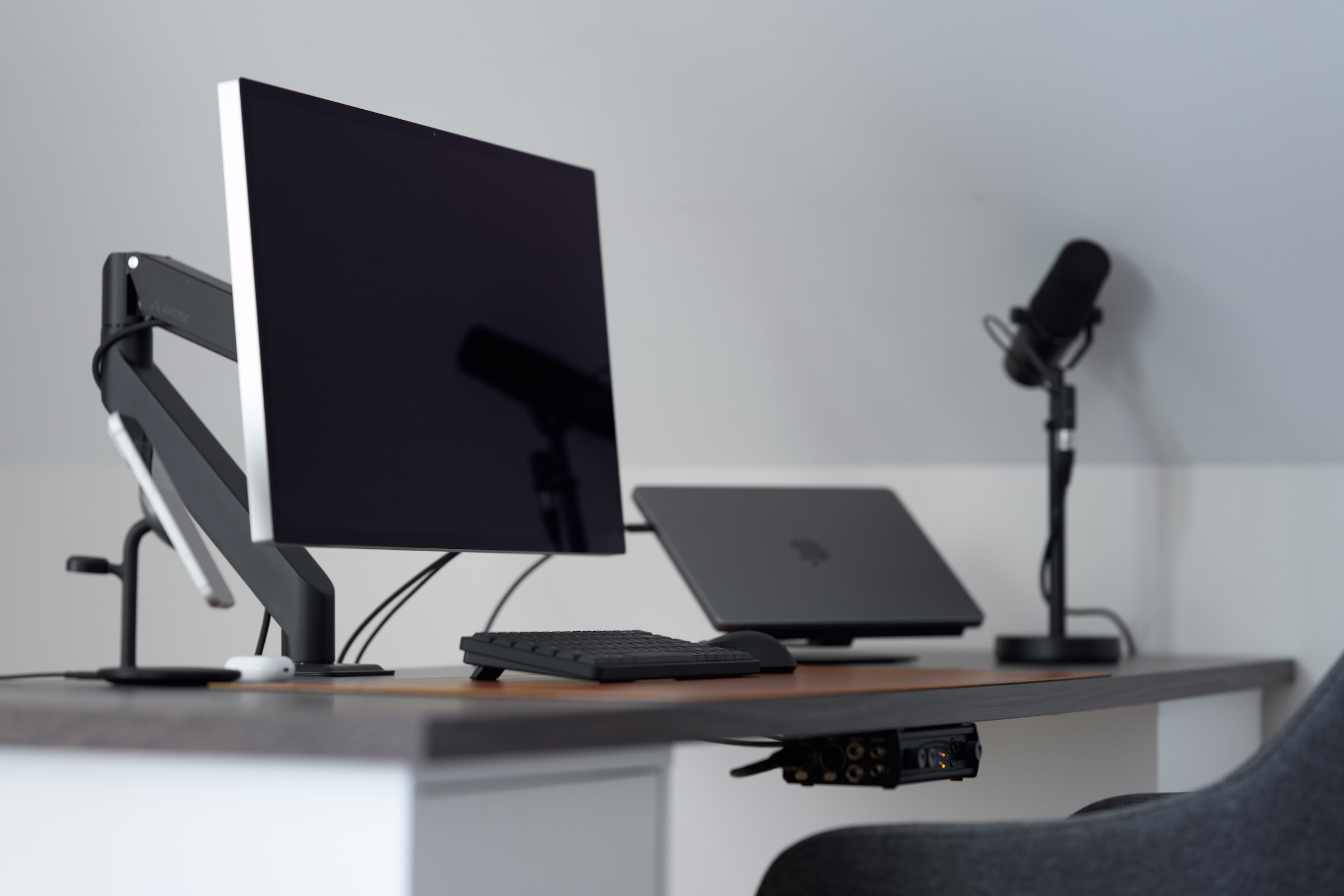 A desk setup with a large monitor, laptop, a microphone, keyboard, and audio interface.