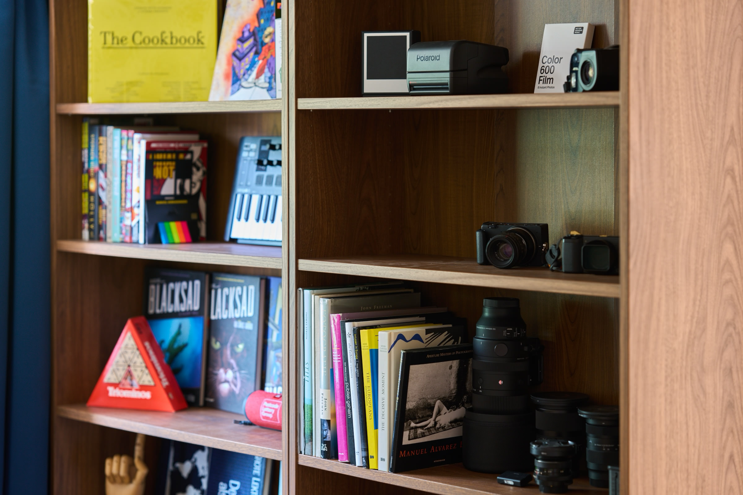 Walnut bookshelf filled with books, a Polaroid camera, lenses, and other photography gear.