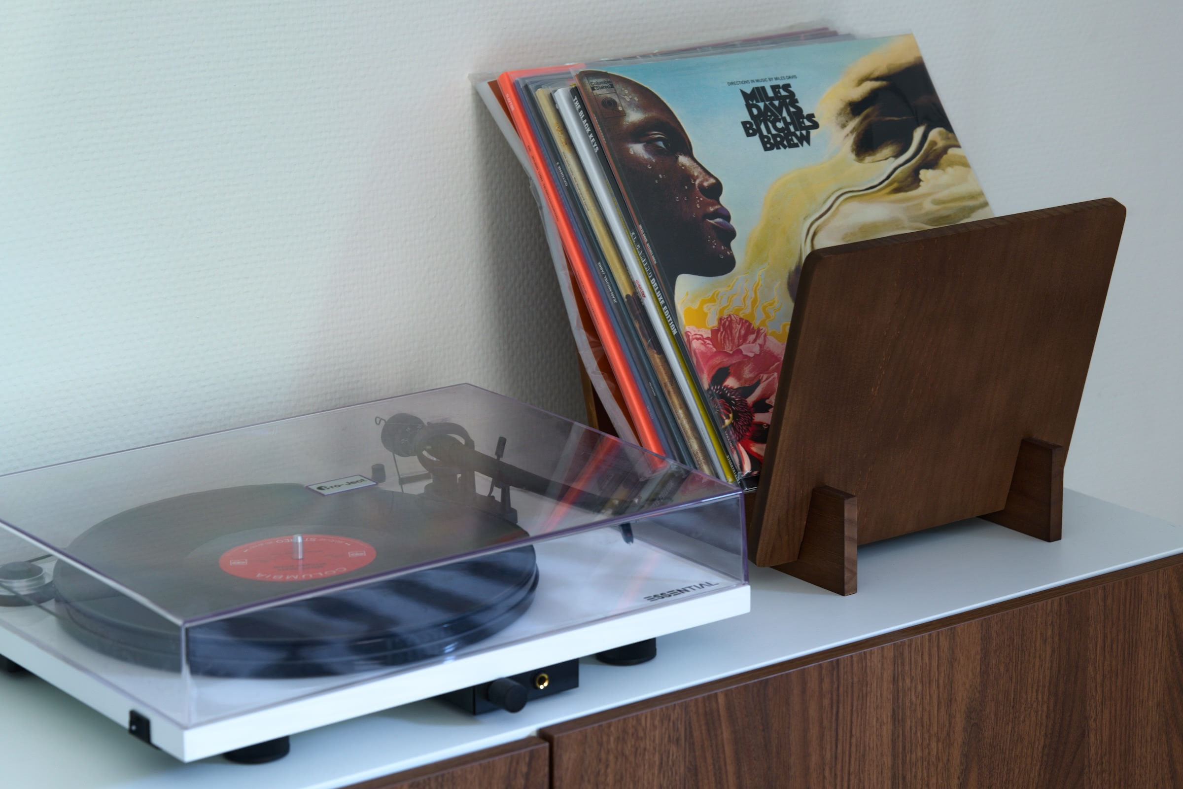 A turntable sits next to a stack of vinyl records in a walnut stand.